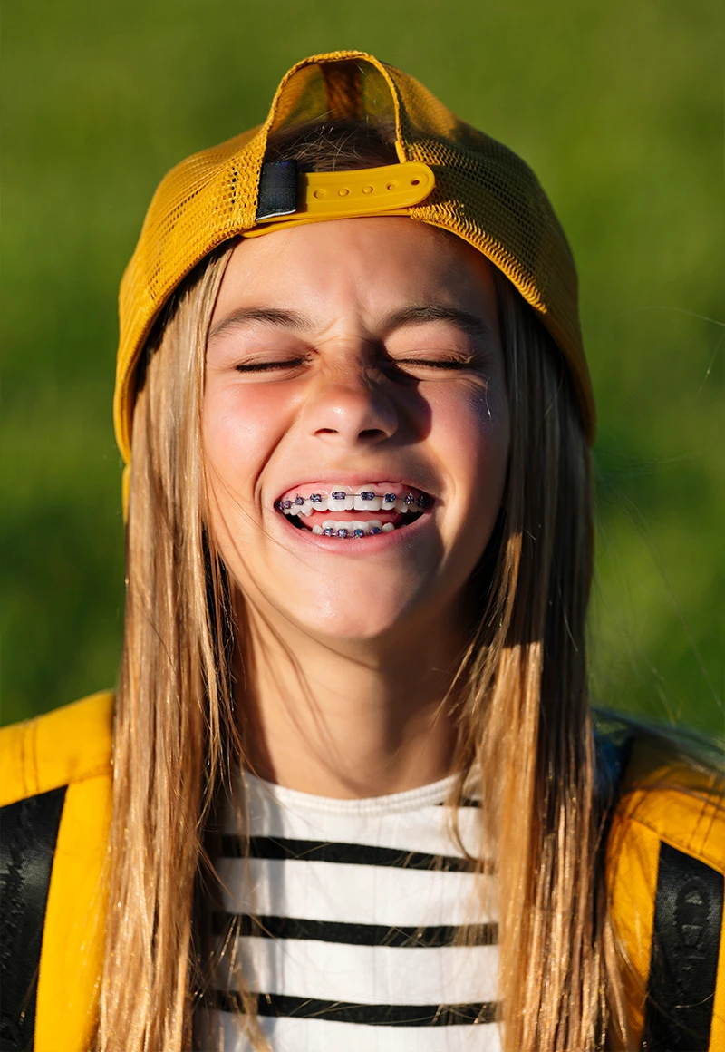 Young girl smiling with colorful braces outdoors, showing orthodontic treatment for kids